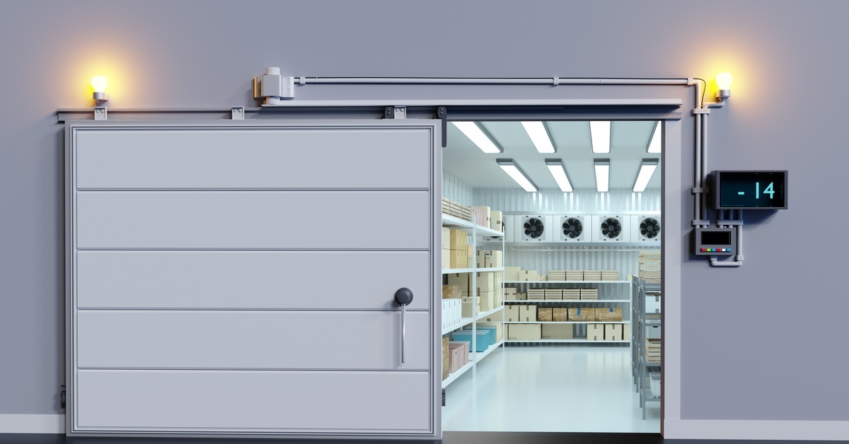 A walk-in cooler with a sliding door. Inside the cooler are several shelves filled with cardboard boxes.