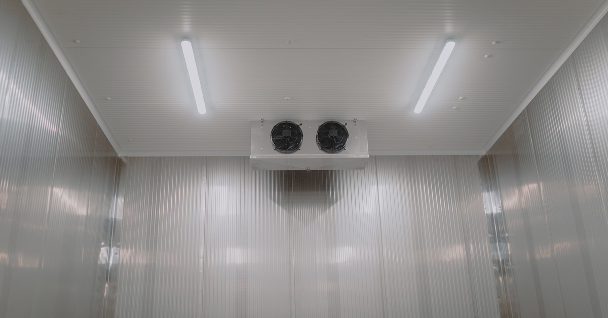 A small walk-in cooler with a refrigeration unit on the ceiling. The walls are covered with ridged aluminum panels.