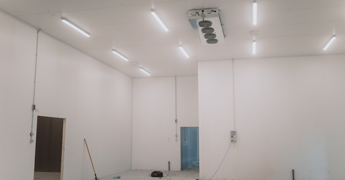 A large open walk-in cooler area with a refrigeration unit on the ceiling. The walls have white panels attached to them.